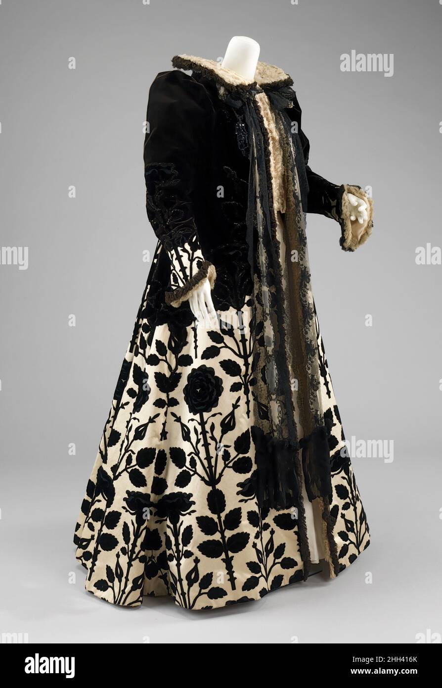 Abendmantel ca. 1900 House of Worth der französische Historismus war ein Hauptmerkmal des House of Worth, beginnend mit dem Interesse von Charles Frederick Worth, historische Kostüme durch Museumsforschung zu studieren. Dieser Abendmantel enthält bereitwillig eine Ikonographie der Tudors mit einem Tudor-Rosenmuster sowie die Silhouette alternativer 16th Century Negligées in den vollen Ärmeln, Stehkragen und untaillierten Stil. Worth manipuliert das Textil genial, um ein völlig neues Muster auf der Rückseite zu schaffen und hat ein scharfes Auge für die Schaffung der subtilen schwarz auf schwarz Muster auf der Oberseite zu kontern Stockfoto