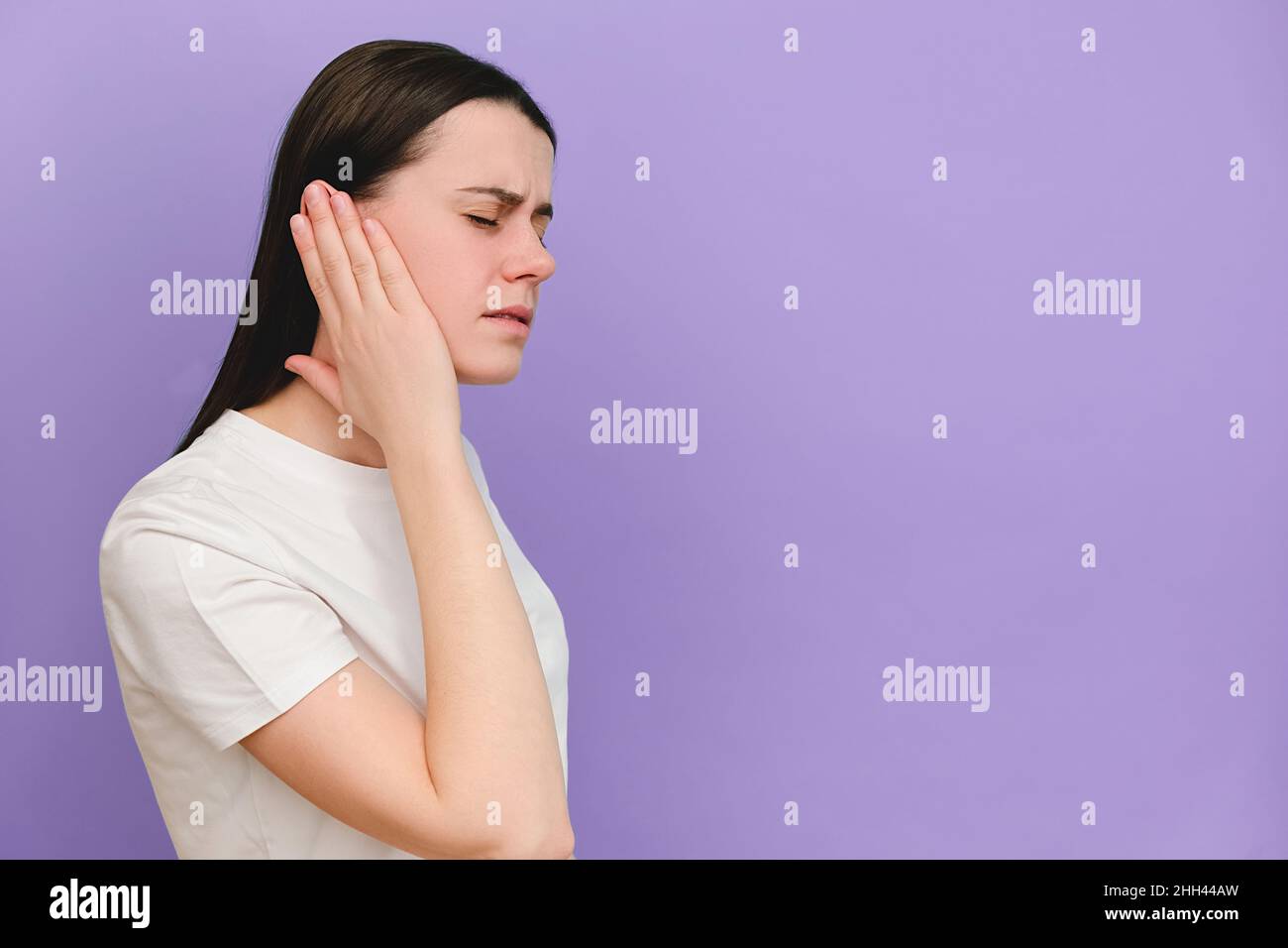 Nahaufnahme von verärgert traurig junge kaukasische Frau mit schmerzhaftem Ohr, plötzlich starke Schmerzen, posiert isoliert auf violetten Hintergrund Wand mit CO Stockfoto