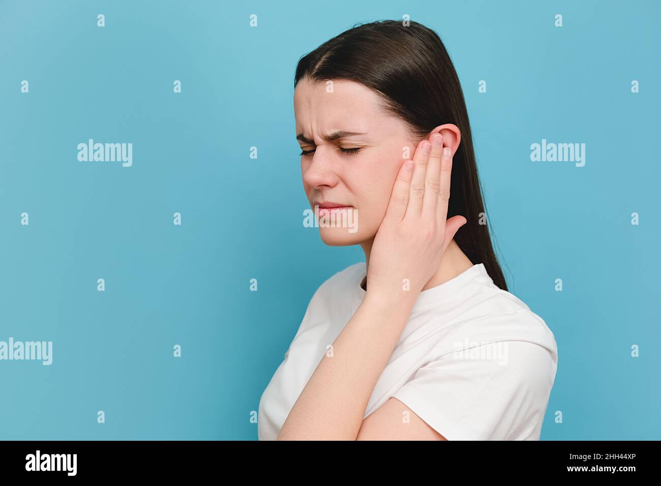 Nahaufnahme von verärgert traurig junge tausendjährige Frau mit schmerzhaftem Ohr, plötzlich starke Schmerzen fühlen, posiert isoliert auf blauem Hintergrund Studio mit Stockfoto
