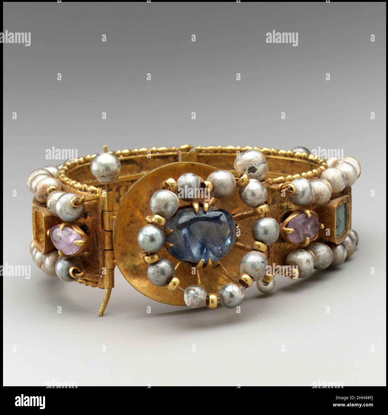Jeweled Bracelet 500–700 Byzantine Diese aufwendig verzierten Armbänder haben reich verzierte Außenflächen und fein detaillierte Opus-Interrasile-Muster auf ihren Innenräumen. Die leuchtende Schönheit der Perlen wurde in der byzantinischen Welt hoch geschätzt. Armband Mit Schmucksteinen. Byzantinisch. 500–700. Gold, Silber, Perle, Amethyst, Saphir, Opal, Glas, Quarz, Smaragdplasma. Hergestellt wahrscheinlich in Konstantinopel. Metallarbeiten-Gold Stockfoto
