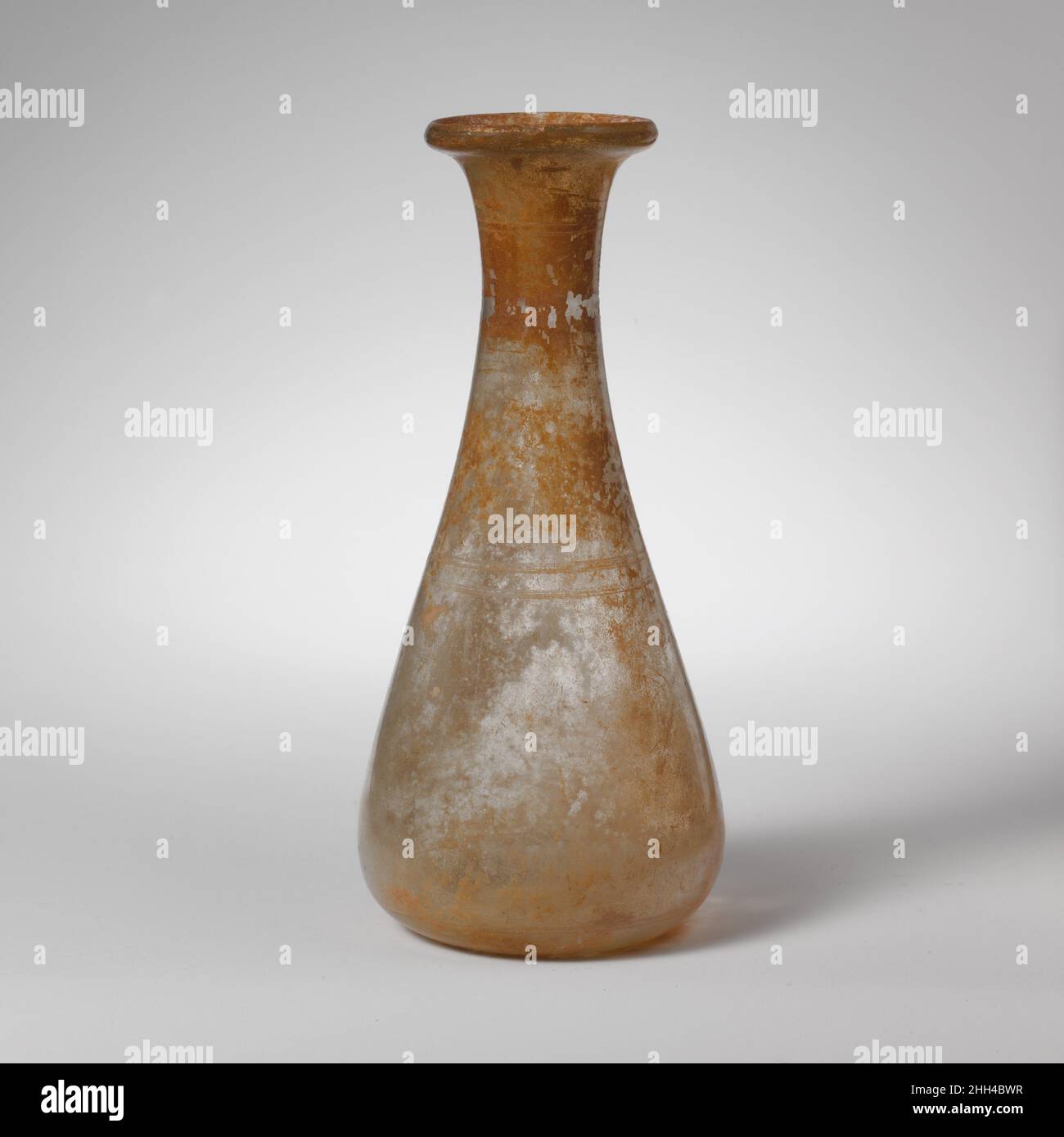 Glaskolben 2nd–3rd century A.D. Roman farblos.Abfackeln, massiver Rand mit abgerundeter Kante am äußeren Rand; konkaver Hals, der sich unmerklich mit schrägen Seiten des Körpers verbindet; konkaver Boden.Radabrieb-Dekoration in drei Gruppen von horizontalen Bändern; Zwei parallele Linien 1,95 und 2,1 cm unter dem Rand, zwei breitere parallele Linien 8,4 und 9,0 cm unter dem Rand, und zwei enge parallele Linien 0,9 und 0,85 über dem Boden.intakt; wenige Blasen, aber ein oder zwei krautige Einschlüsse; Flecken von Schillern und emaillartigen Verwitterung. Glaskolben 239609 Stockfoto