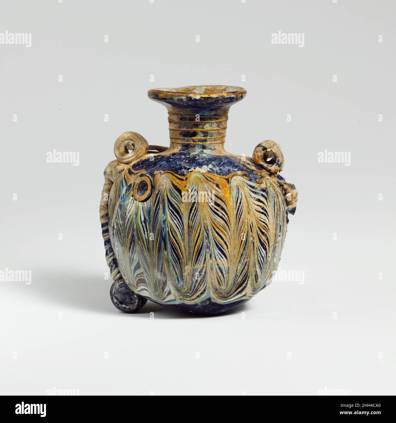 Glaslentoid Aryballos (Parfümflasche) Ende 4th–Anfang 3rd Jahrhundert v. Chr. östliches Mittelmeer oder Italienisch Durchscheinendes Kobaltblau, mit Griffen, Rollen und Füßen in gleicher Farbe; Spuren in undurchsichtigem Gelb, undurchsichtigem Weiß und undurchsichtigem Türkisblau.Breite Randscheibe, nach innen geneigt, als Spiralspule um den Hals herum gemacht; Zylindrischer Hals, nach unten zulaufend; breite, fast horizontale Schulter mit abgerundeter Außenkante; abgeflachte Kugelform, mit konvexen Seiten; flacher konvexer Boden; zwei gerollte zylindrische Füße auf beiden Seiten des Bodens; zwei vertikale Ringgriffe an der Schulter befestigt; zwei Rollen laufen Stockfoto