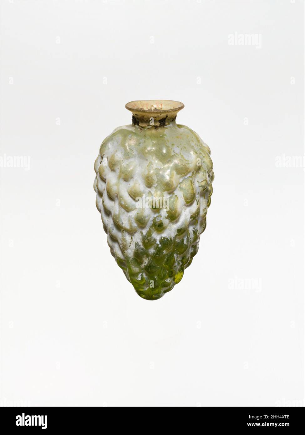 Glaskolben in Form eines Kiefernkegels 2nd Hälfte des 1st. Jahrhunderts n. Chr. römisch lichtdurchlässig hellgrün.einfacher, ausgestreckter Rand; kurzer zylindrischer Hals; eingeschobene Schulter; länglicher Körper mit konvexer Seite, die sich bis zu einem dicken, spitzen Boden verjüngt. Zwei Schimmelnähte verlaufen an den Seiten des Körpers nach unten.Körper mit zehn überlappenden Reihen tropfenförmiger Knöpfe verziert, die vielleicht einen Kiefernkegel darstellen sollen.intakt; stumpfend, weißlich schillernde Verwitterung und Bodenverkrustungen im Inneren. Glaskolben in Form eines Kiefernkegels 249486 Stockfoto