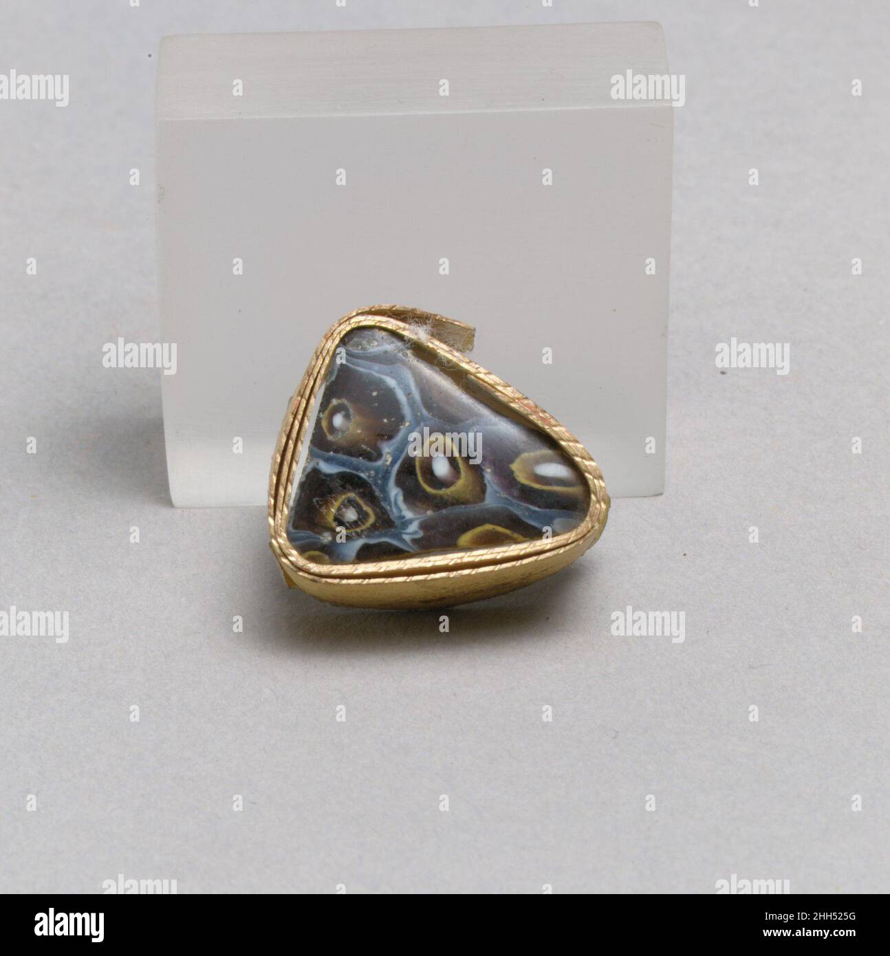 Glasmosaikfragment Ende des 1st. Jahrhunderts v. Chr.–Anfang des 1st. Jahrhunderts n. Chr. Römisches dünnwandiges Randfragment. Halbopakes graublaues, durchscheinendes tiefviolettes, opakes Weiß und Gelb. Vertikaler, abgeschrägter Rand; Fast gerade Seite, nach unten verjüngend.Mosaikmuster aus polygonalen Abschnitten eines einzelnen Rohres in einem violetten Boden in weiß umrandet und umgeben von einem unregelmäßigen blauen Band, einem gelben Kreis in einem violetten Boden mit einem zentralen weißen Stab; auf dem Inneren, horizontal geschnittenes Band unter dem Rand.poliert außen; Lochfraß und Verwitterung von Oberflächenblasen; Abstumpfen, Lochfraß und cremige Verwitterung auf dem Innenraum, dem Rand Stockfoto