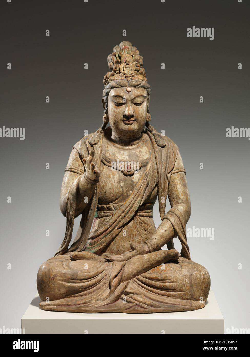 Bodhisattva Avalokiteshvara (Guanyin) Ende des 10th.–Anfang des 11th. Jahrhunderts China Es ist selten, eine Skulptur von Avalokiteshvara zu finden, die wie in der Meditation sitzend mit seinen Beinen gefaltet ist. Meistens wird er stehend oder sitzend mit einem gebeugten Bein und dem anderen hängenden Bein gezeigt – eine Pose, die als „königliche Leichtigkeit“ bekannt ist. Eine Ausnahme ist, wenn Avalokiteshvara in Szenen des Reinen Landes des Buddha Amitabha erscheint. Es ist möglich, dass diese Skulptur Teil einer solchen Komposition war. Bodhisattva Avalokiteshvara (Guanyin). China. Ende des 10th.–Anfang des 11th. Jahrhunderts. Holz (Fuchshandschuh) mit Pigmenten, Vergoldung, Quarz und Karneol; Einzelholz Stockfoto