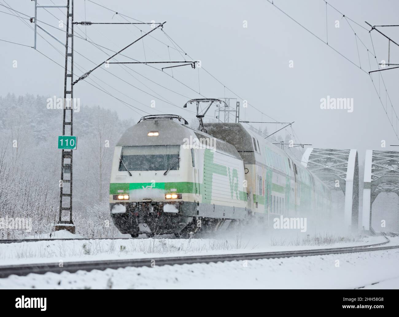 Personenzug bei starkem Schneefall, der aus der Eisenbahnbrücke kommt Stockfoto