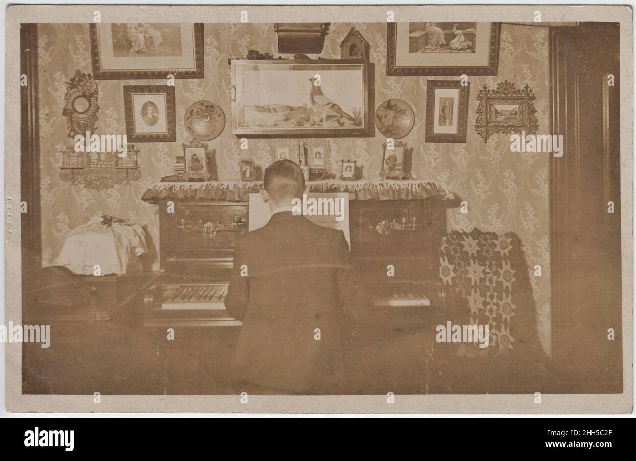 In einem edwardianischen Mittelklassehaus, mit Blick auf den Rücken eines Mannes, der auf einem aufrechten Klavier praktiziert. Die Wand ist mit Porträts und anderen Ornamenten bedeckt Stockfoto