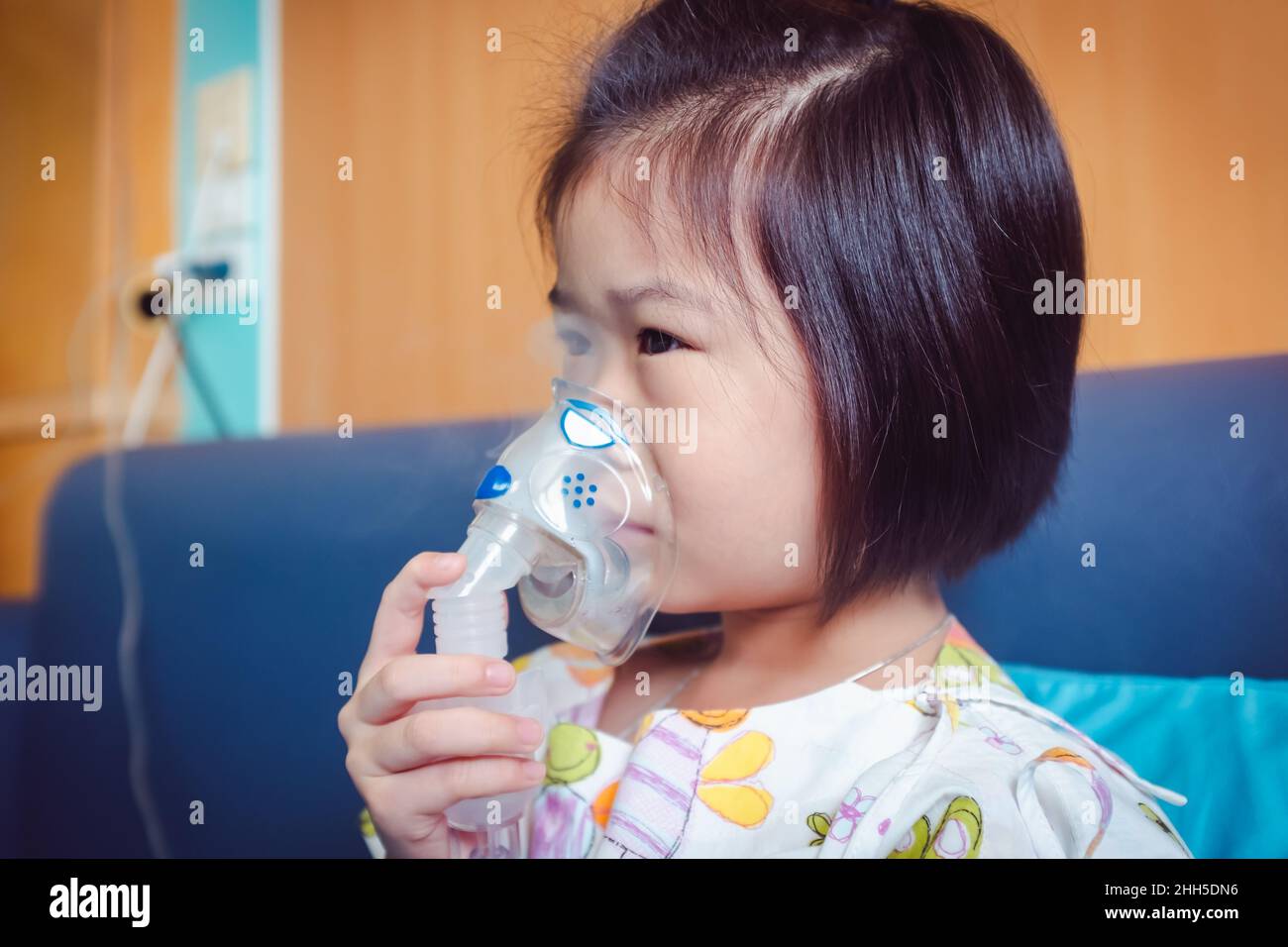 Trauriges asiatisches Kind hält einen Maskendampf-Inhalator zur Behandlung von Asthma. Atmung durch einen Dampfvernebler.Krankheit Mädchen im Krankenhaus eingeliefert. Stockfoto