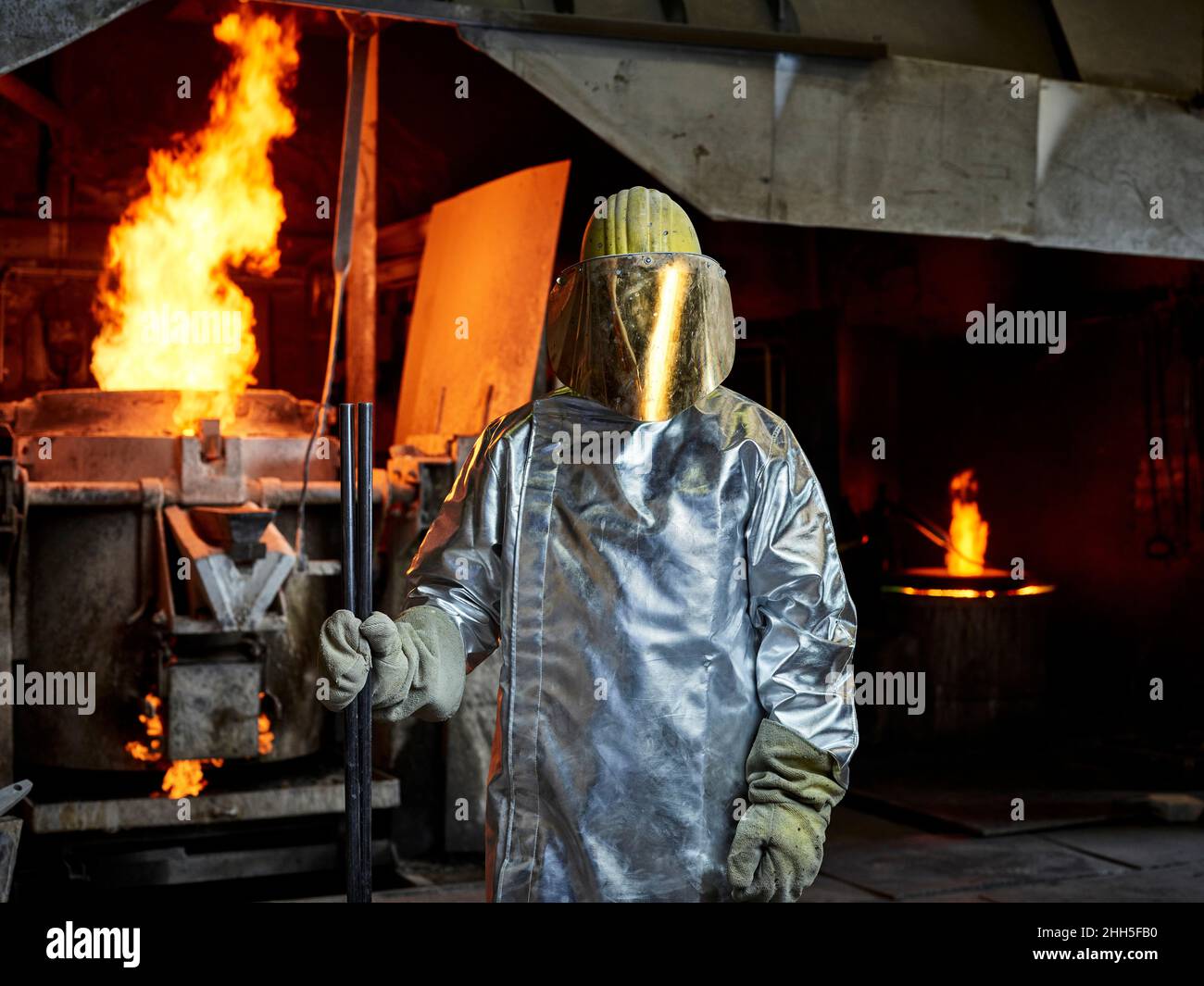 Gießerei Arbeiter tragen Schutzhelm mit Gesichtsschutz stehen in brennender Fabrik Stockfoto