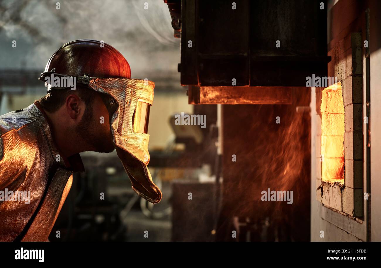 Arbeiter mit blauem Kragen, der Schutzhelm trägt und den brennenden Ofen in der Industrie betrachtet Stockfoto