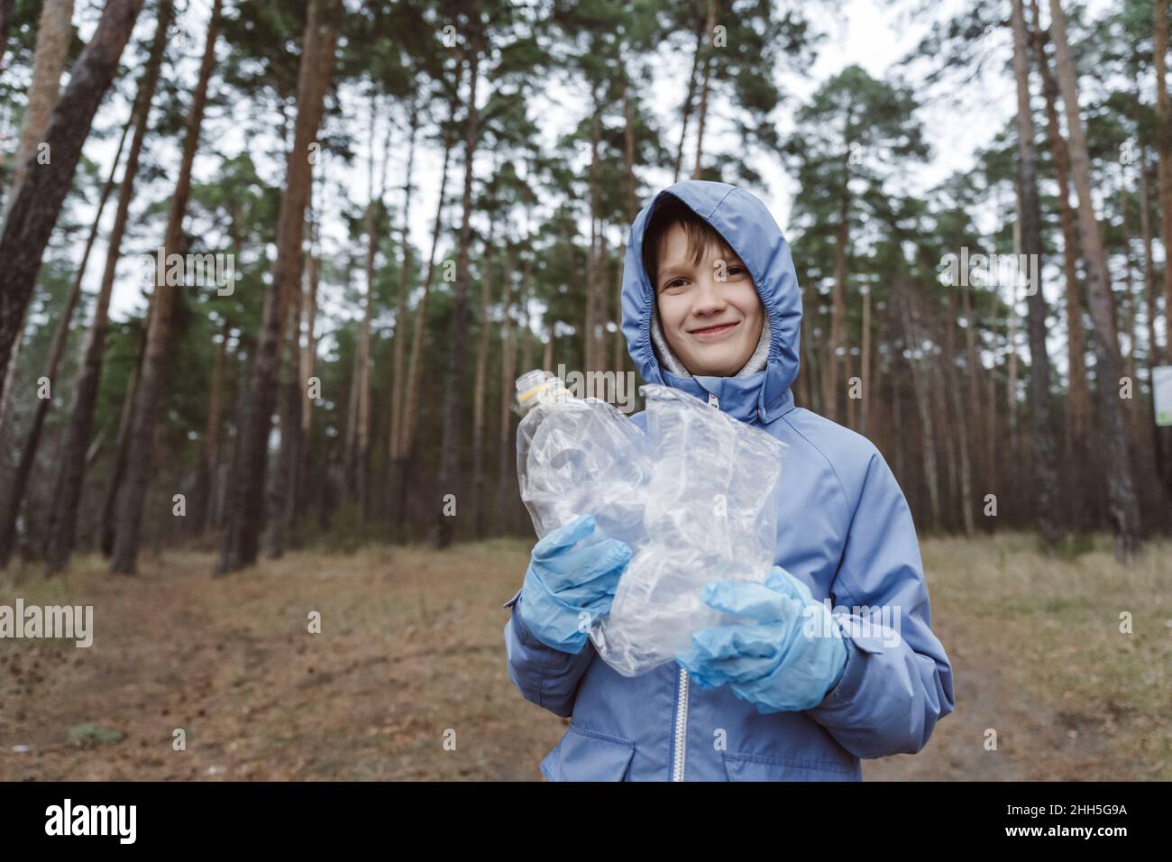Lächelnder Junge hält Plastikmüll im Wald Stockfoto