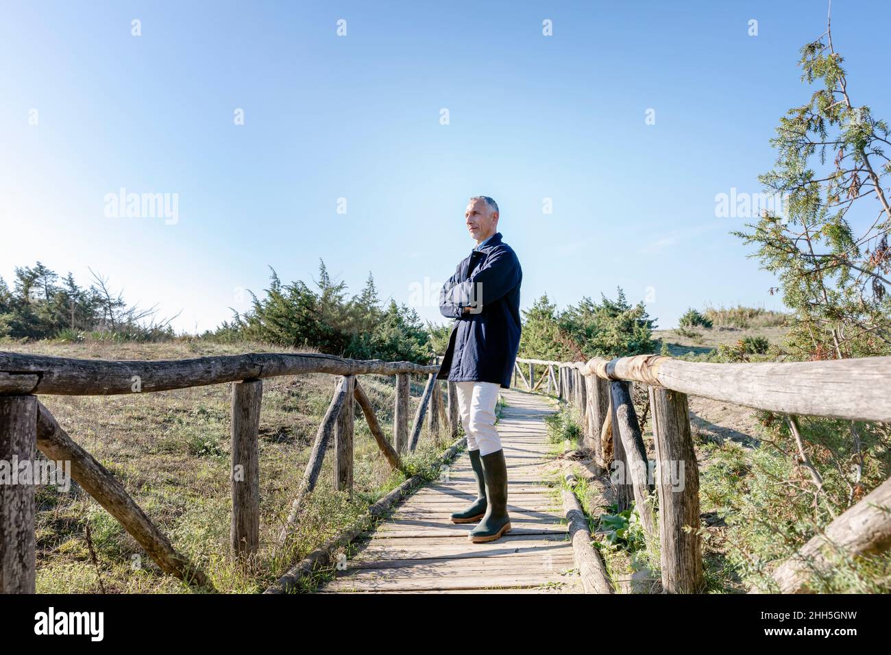 Mann, der mit gekreuzten Armen auf einer Holzbrücke steht Stockfoto