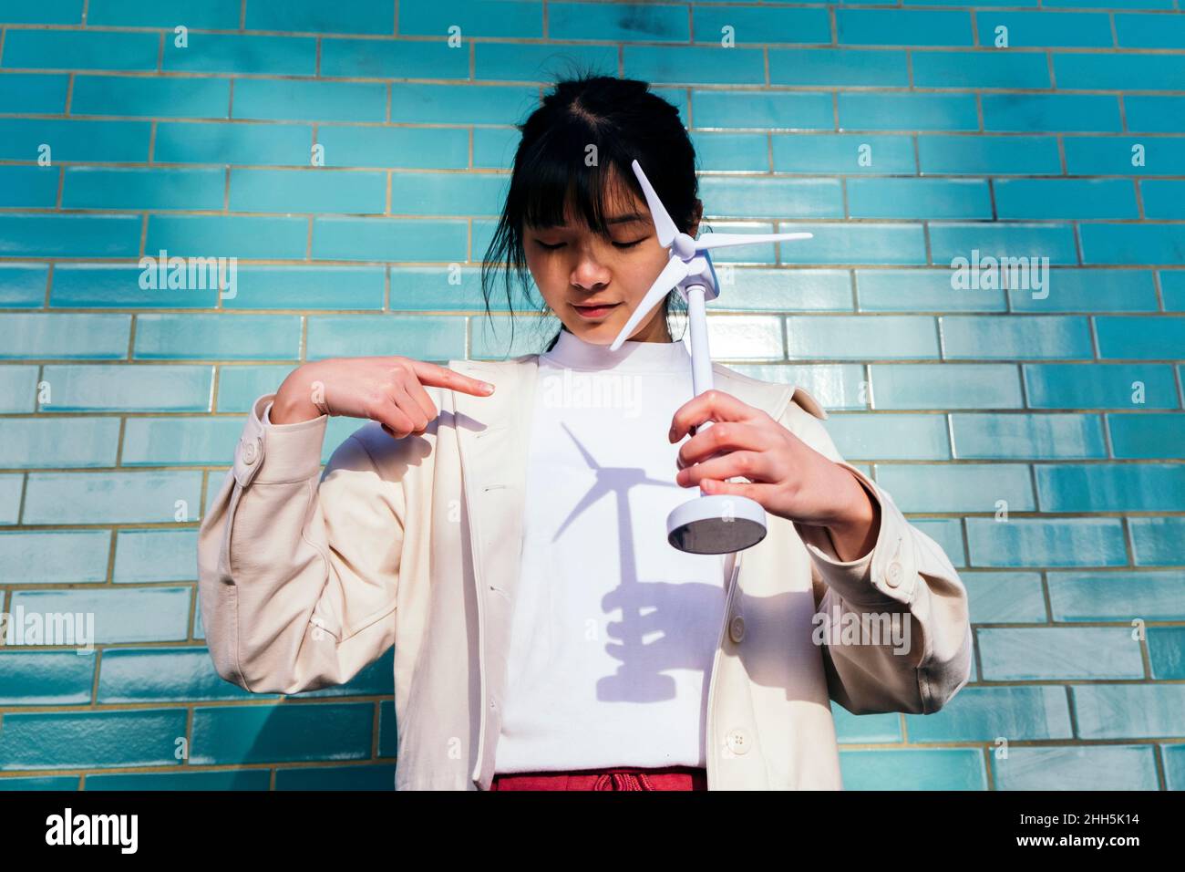 Junge Frau, die auf den Schatten der Windturbine auf dem T-Shirt vor der Backsteinmauer zeigt Stockfoto