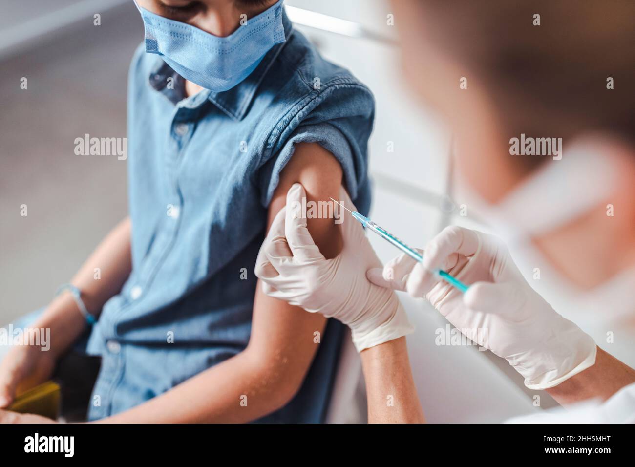 Krankenschwester, die einen Jungen mit Gesichtsmaske im Gesundheitszentrum impft Stockfoto