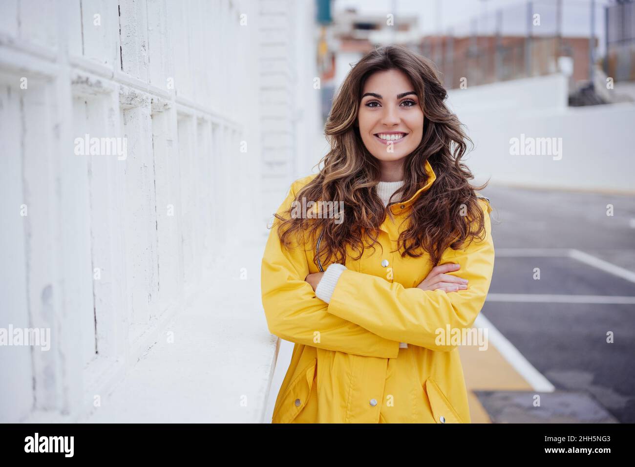 Lächelnde Frau, die mit den Armen, die von der Wand gekreuzt sind, steht Stockfoto
