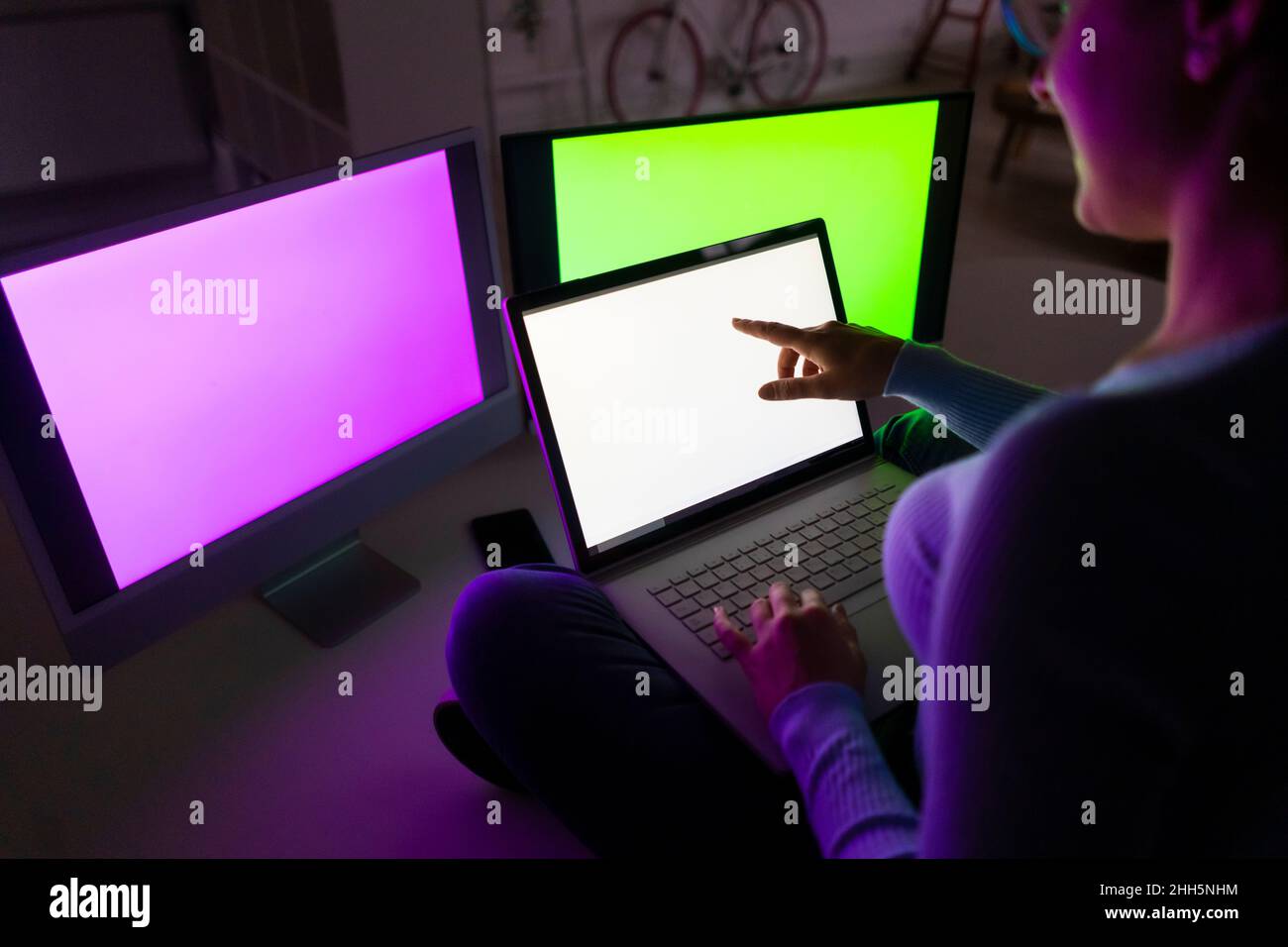 Geschäftsfrau mit Laptop sitzt vor beleuchteten leeren Bildschirmen im Heimbüro Stockfoto