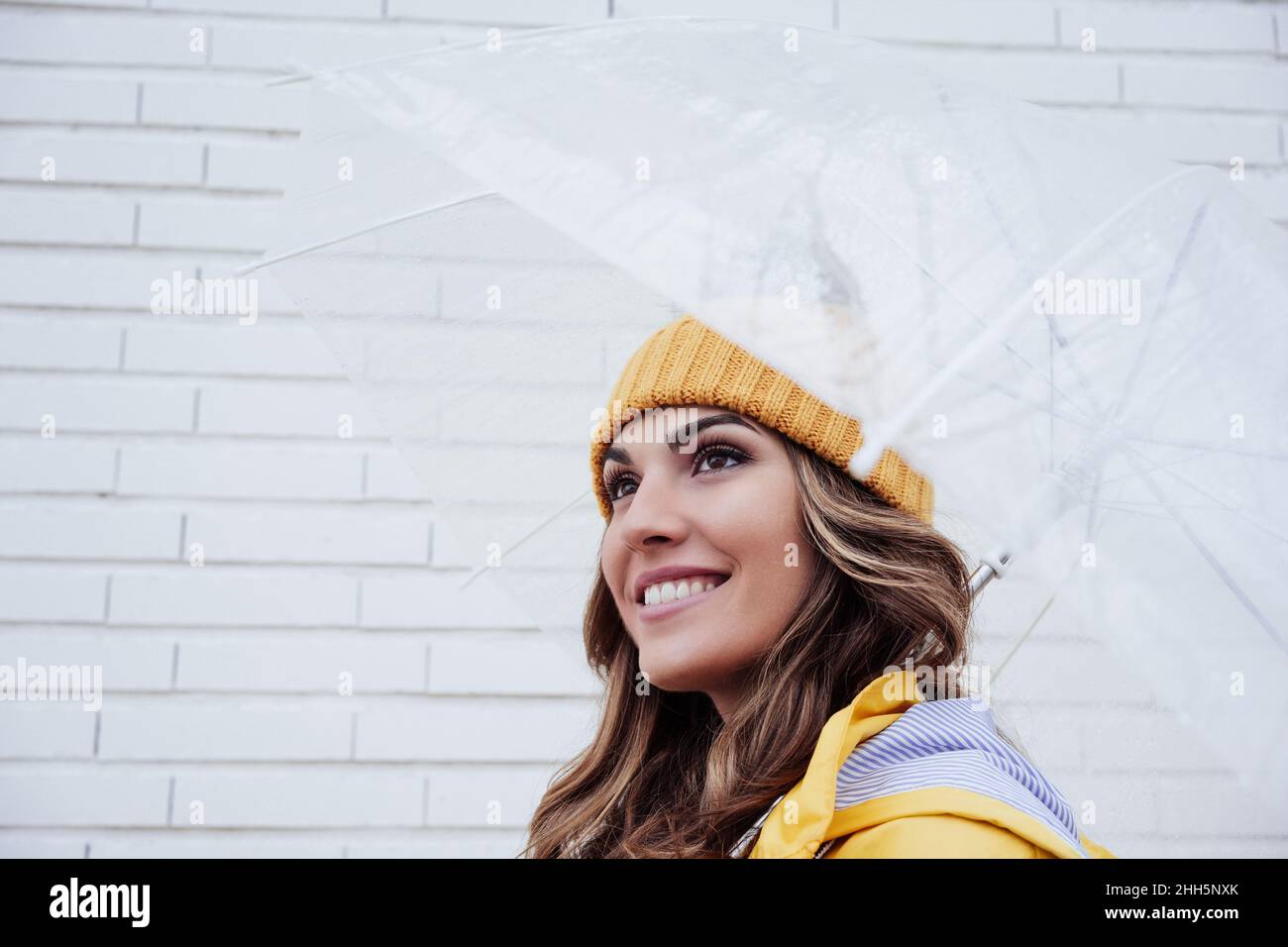 Lächelnde Frau mit transparentem Schirm an der Wand Stockfoto