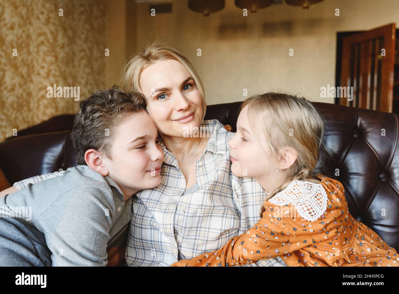 Lächelnde Mutter mit Tochter und Sohn, die zu Hause auf dem Sofa sitzen Stockfoto