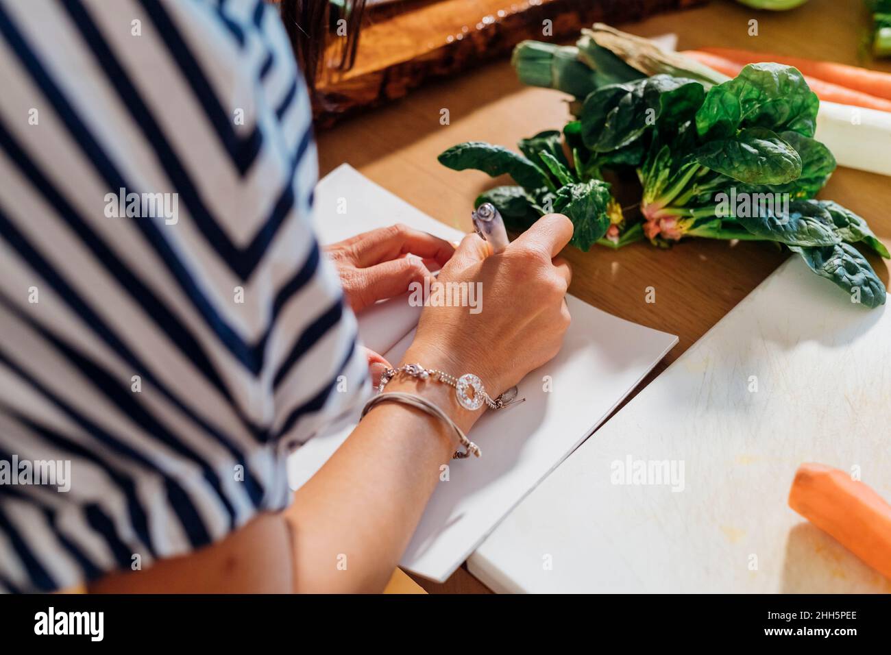 Frau schreibt Rezept in Notizblock auf Tisch zu Hause Stockfoto