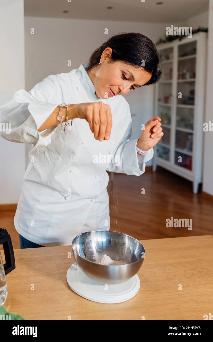 Koch fügt zu Hause eine Prise Salz in eine Stahlschüssel auf den Tisch Stockfoto