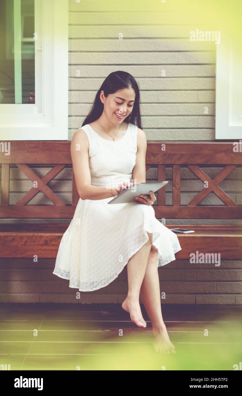 Asiatische junge Frau mit digitalen Tablet draußen auf zu Hause Sommer. Aktiver Lebensstil glücklicher junger Erwachsener an einem entspannenden Tag zu Hause. Vintage-Ton. Stockfoto
