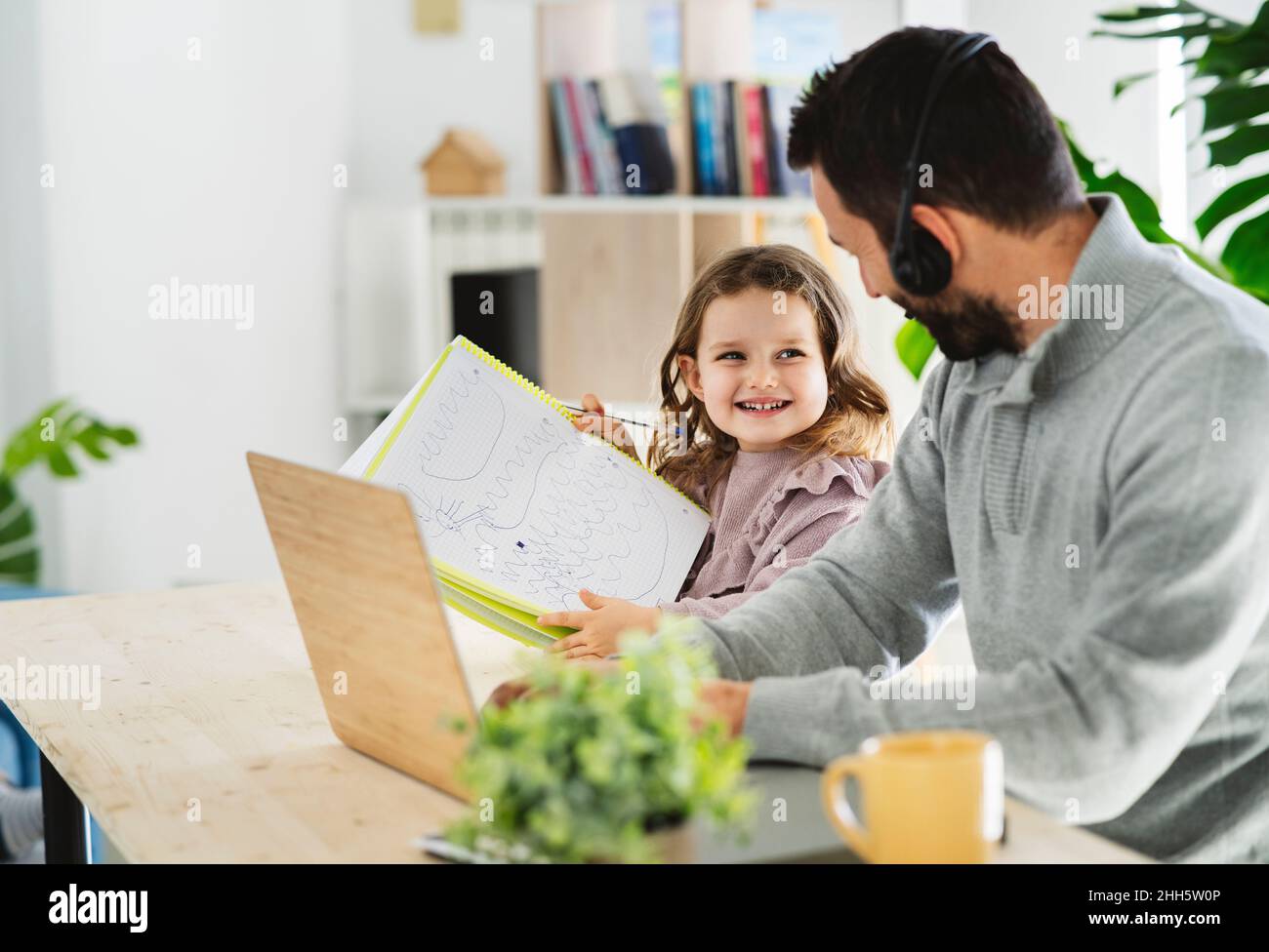 Lächelndes Mädchen, das dem Vater, der zu Hause arbeitet, eine Zeichnung zeigt Stockfoto