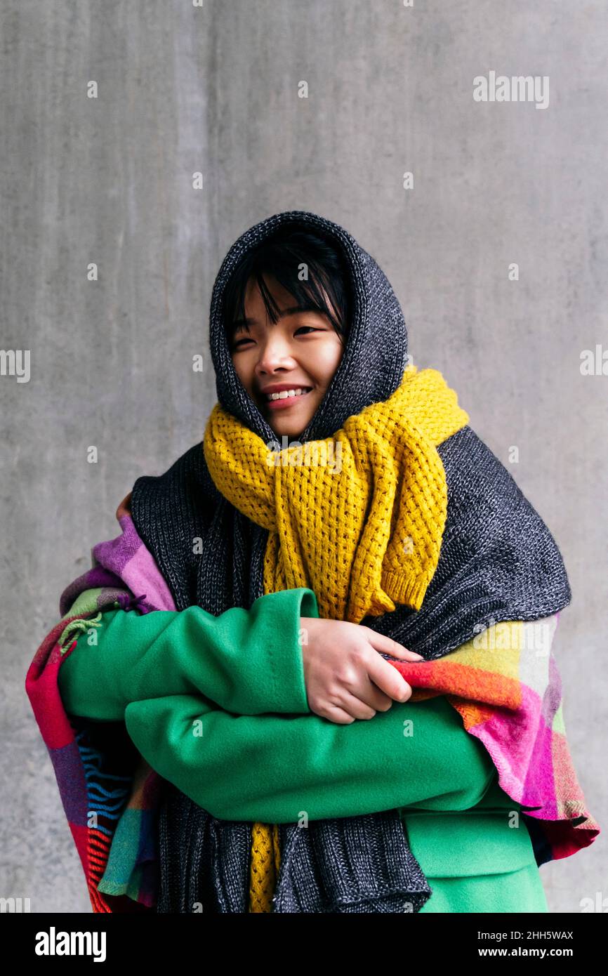 Lächelnde Frau in warmer Kleidung, die in eine Decke gehüllt ist Stockfoto