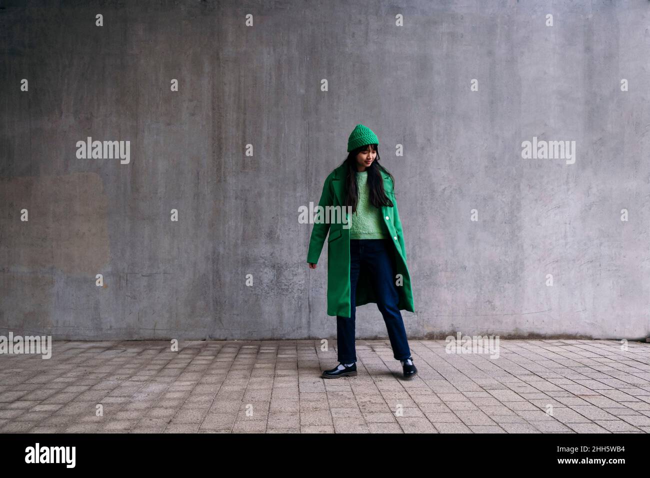 Junge Frau im grünen Wintermantel, die auf dem Fußweg steht Stockfoto