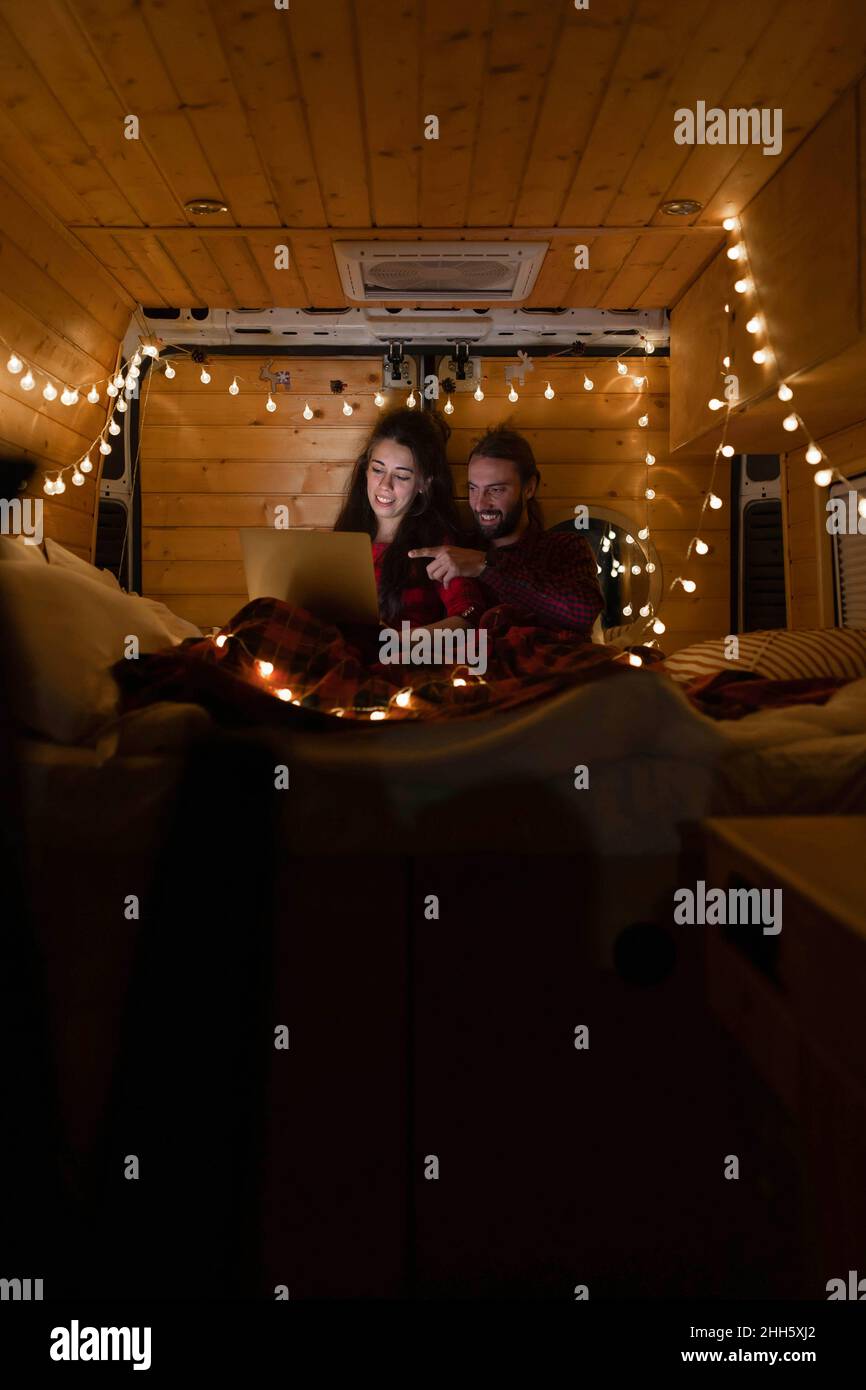 Junger Mann, der auf den Laptop zeigt, mit Freundin im Van im Urlaub Stockfoto