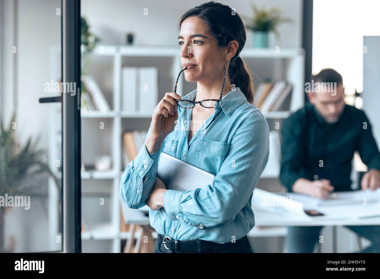 Kontemplative Geschäftsfrau mit Brille in kleinem Büro Stockfoto