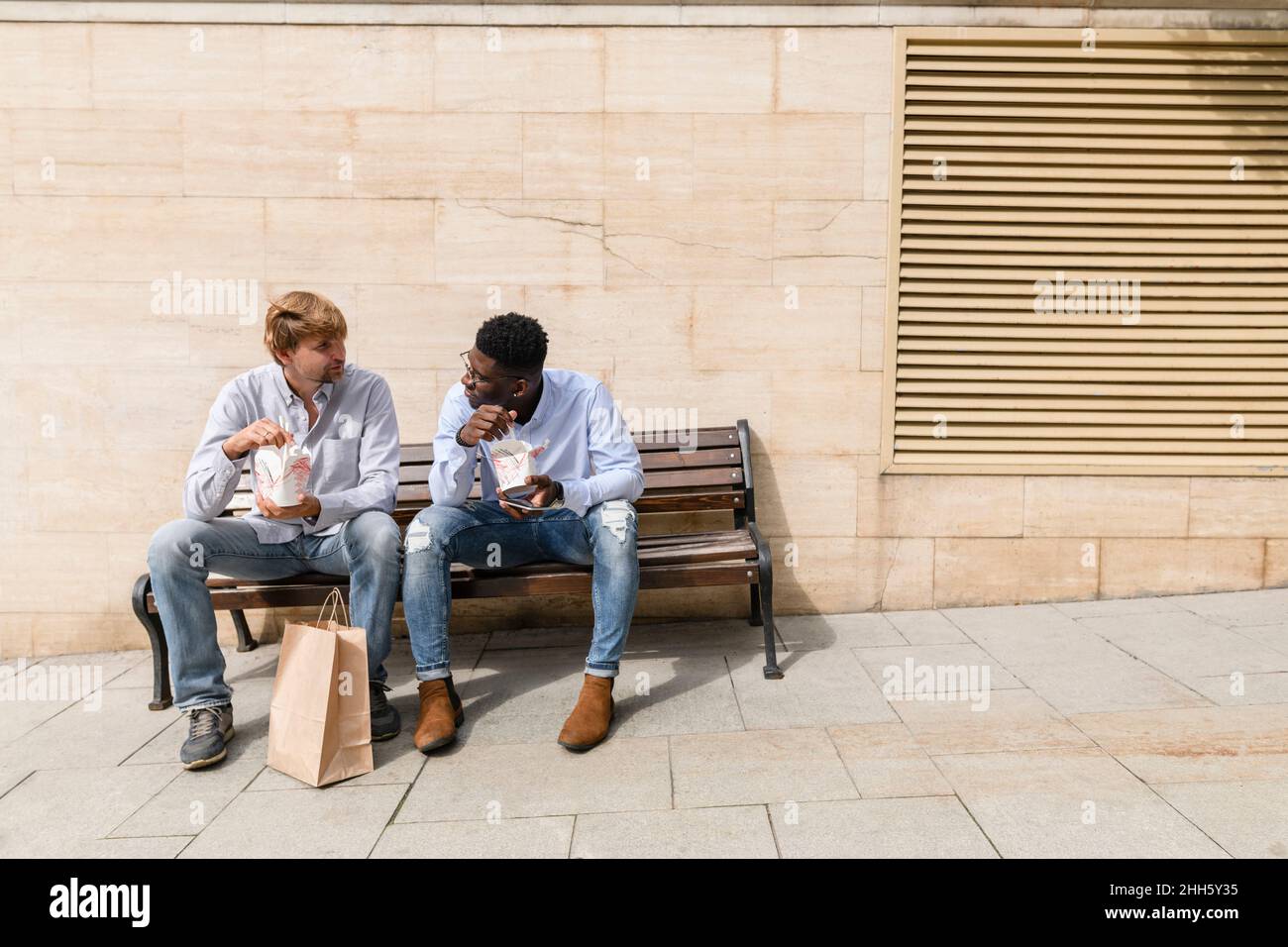 Multirassische Freunde sprechen und essen auf der Bank Stockfoto