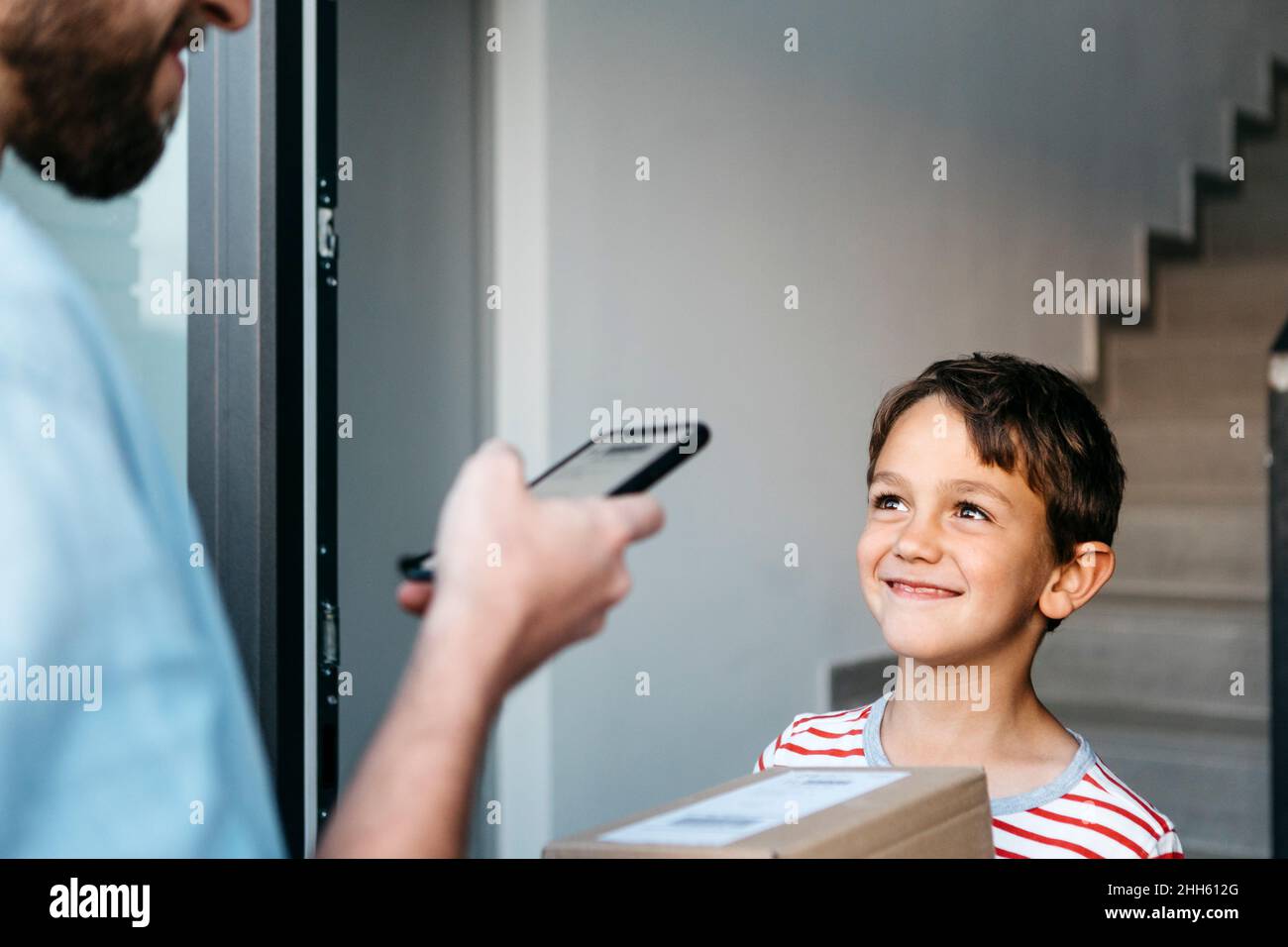 Lächelnder Junge, der den Lieferer ansieht, der den Barcode auf dem Paket scannt Stockfoto