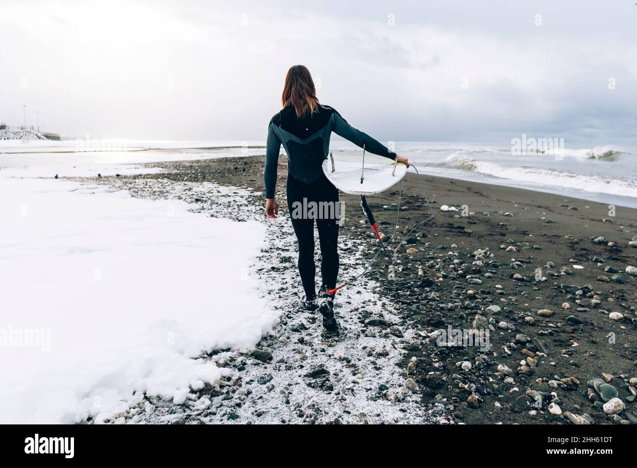 Mann mit Surfbrett läuft am verschneiten Strand Stockfoto