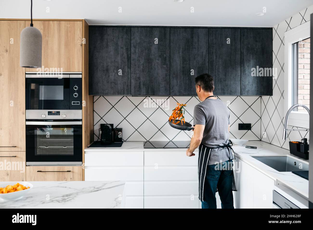 Mann wirft Gemüse in der Pfanne und bereitet das Essen zu Hause zu Stockfoto