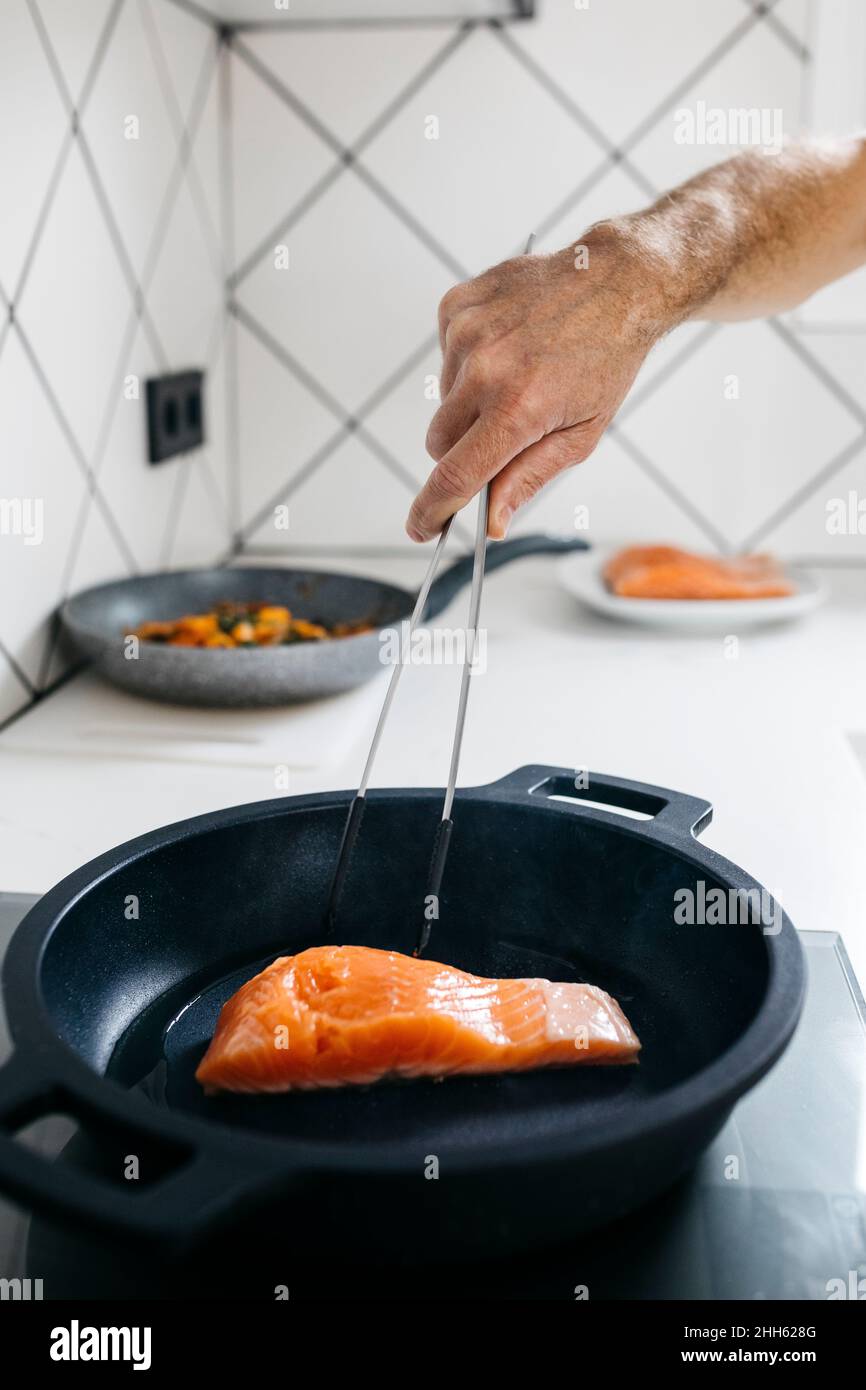 Mann, der zu Hause Fisch mit Zange in der Pfanne kocht Stockfoto