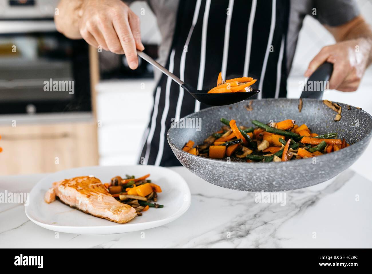 Mann, der zu Hause gebratene Karotten mit Fisch auf den Teller legt Stockfoto