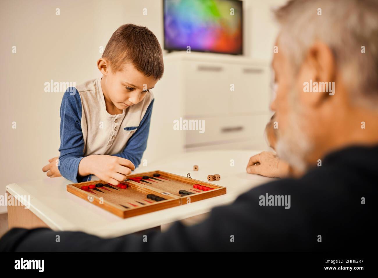 Konzentrierter Junge spielt Backgammon mit Großvater zu Hause Stockfoto