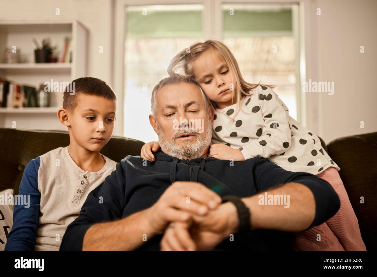 Großvater mit intelligenter Uhr sitzt mit Enkeln zu Hause Stockfoto