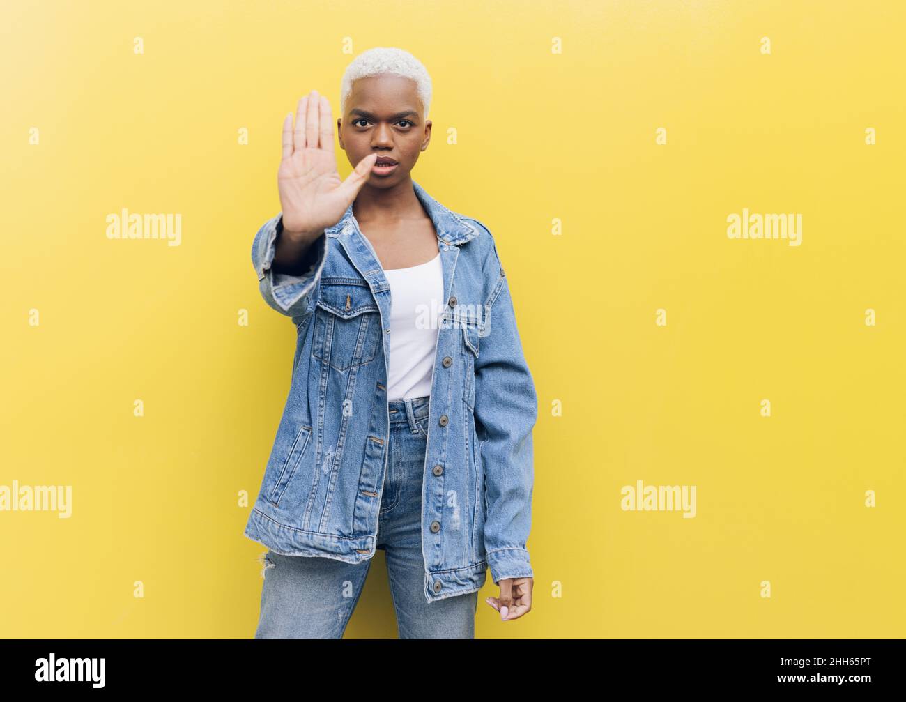 Seriöse Frau macht Stop-Geste stehen vor gelbem Hintergrund Stockfoto