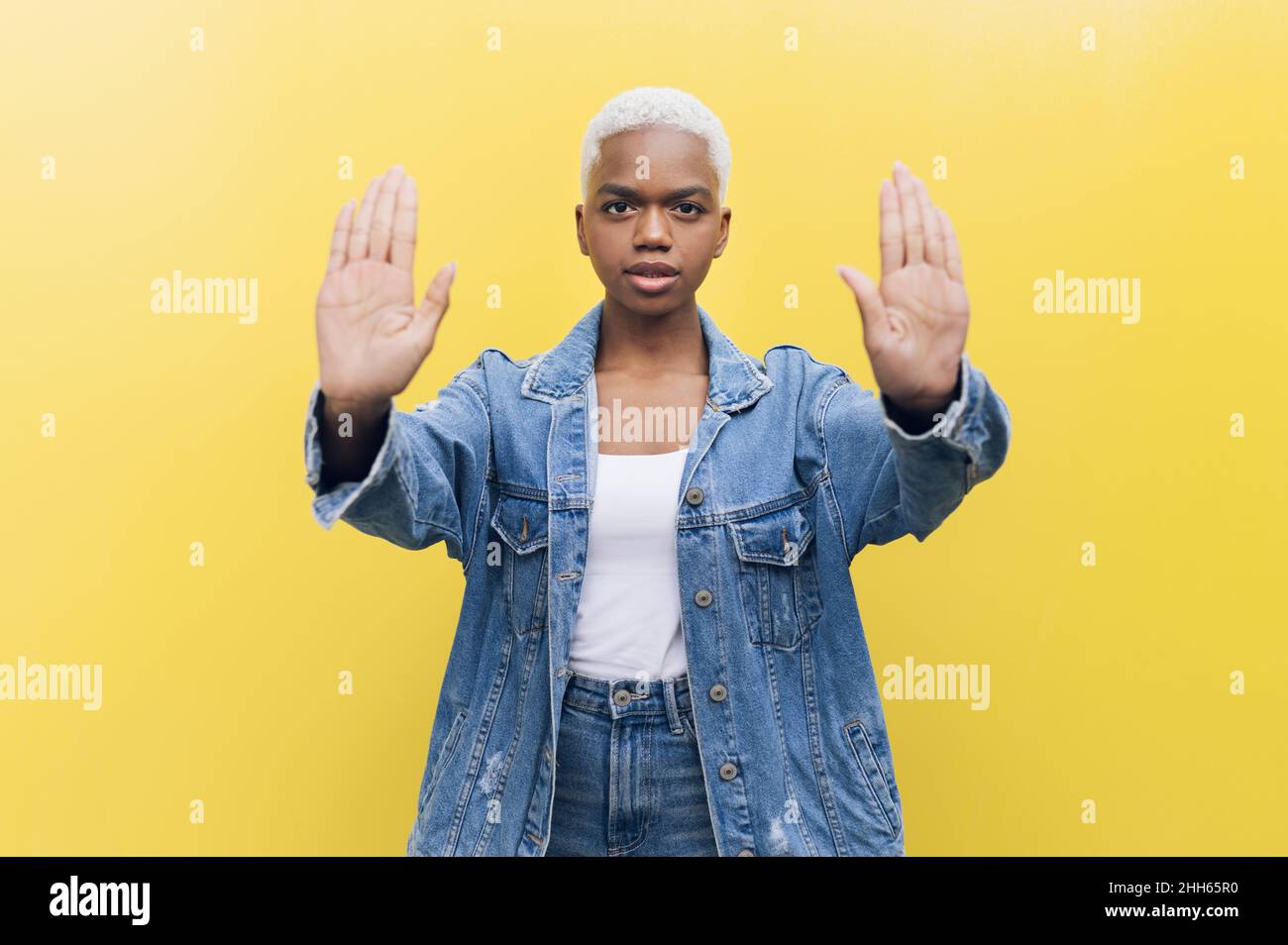 Frau zeigt Stoppgeste mit beiden Handflächen vor gelbem Hintergrund Stockfoto