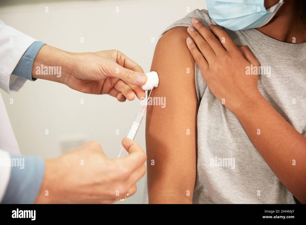 Arzt injiziert dem Mädchen durch eine Spritze im medizinischen Raum eine COVID-19-Impfung Stockfoto