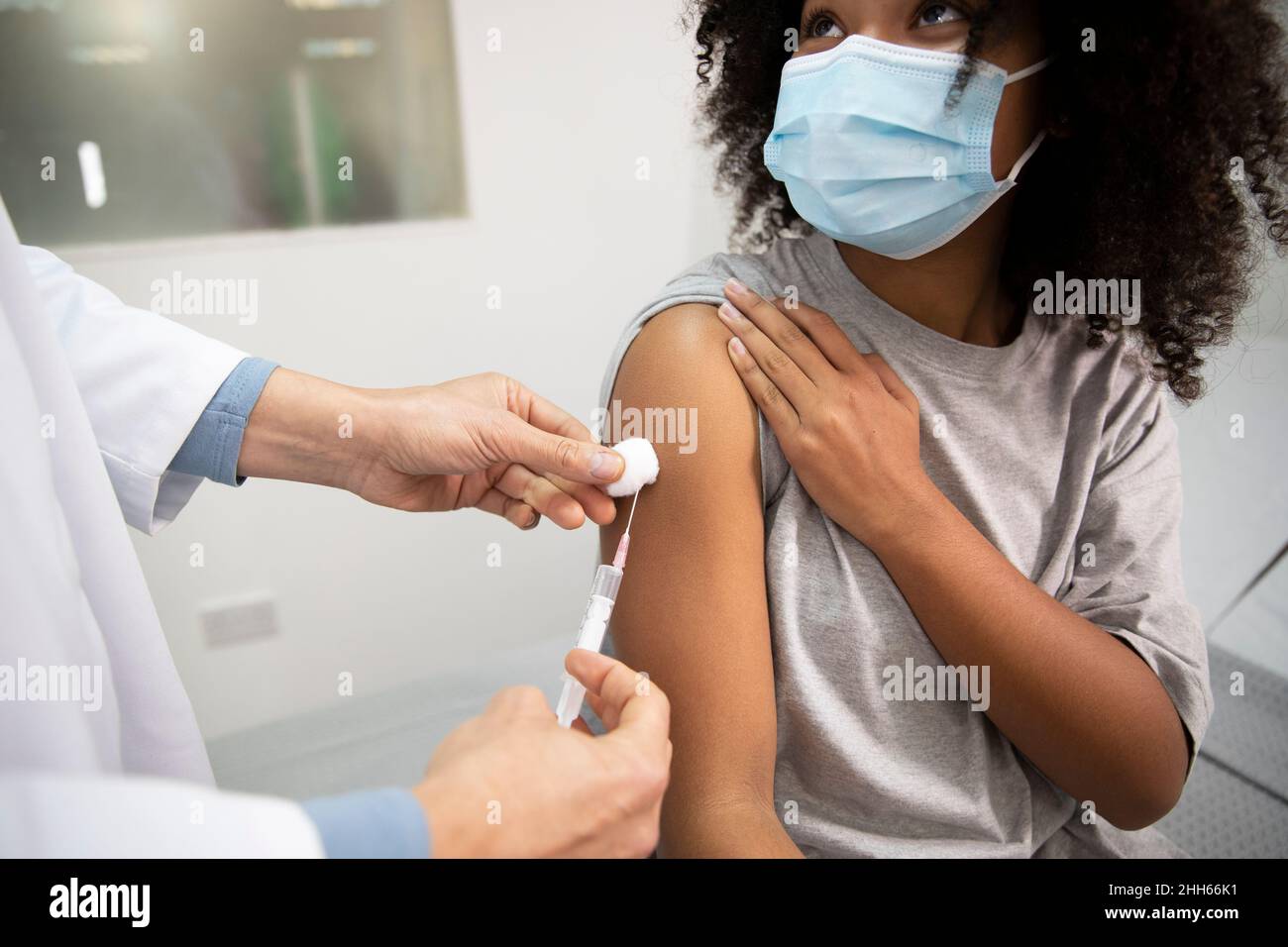 Arzt injiziert COVID-19-Impfung an Mädchen, das eine schützende Gesichtsmaske im medizinischen Raum trägt Stockfoto