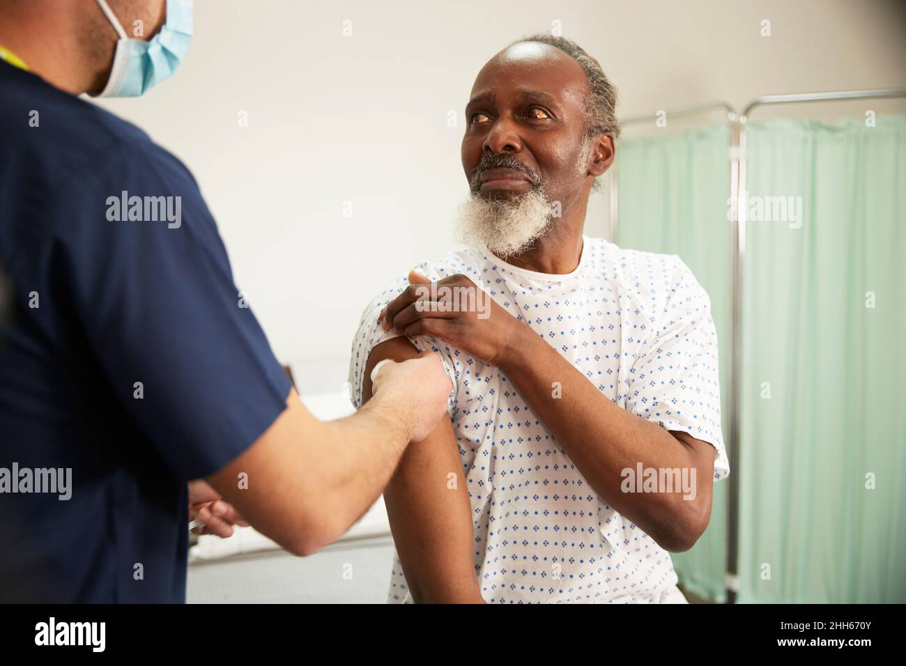 Besorgter Patient, der die Krankenschwester ansieht, die seinen Arm im medizinischen Raum desinfiziert Stockfoto