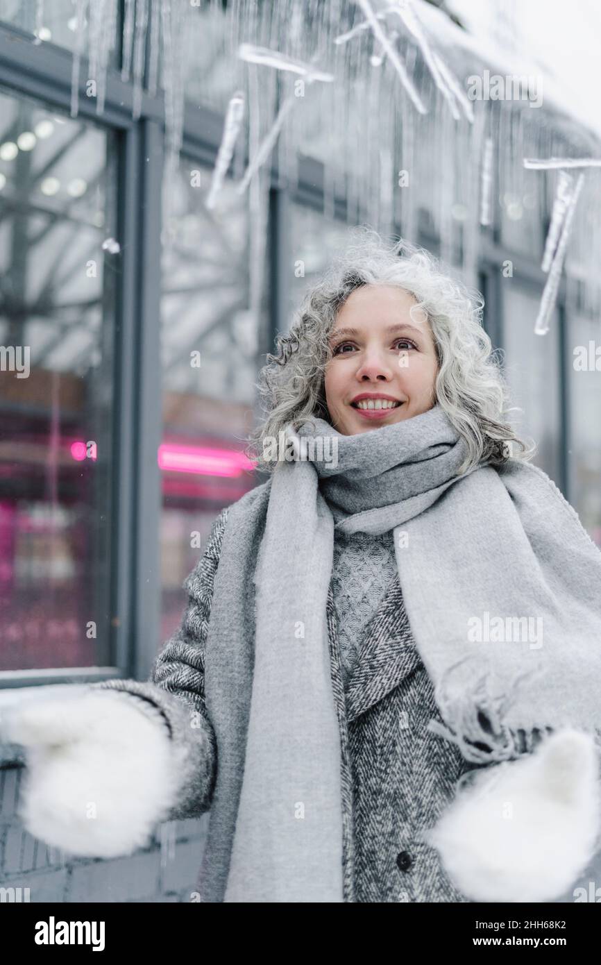 Glückliche Frau in grauer warmer Kleidung, die Eiszapfen wirft Stockfoto