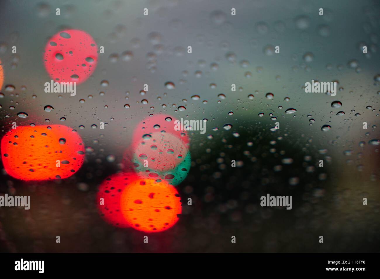 Ampelbokeh mit Regentropfen. Reflexionen von Regentropfen auf Glas auf dem Autofenster. Nachts regnen Tropfen auf das Glasfenster. Stockfoto