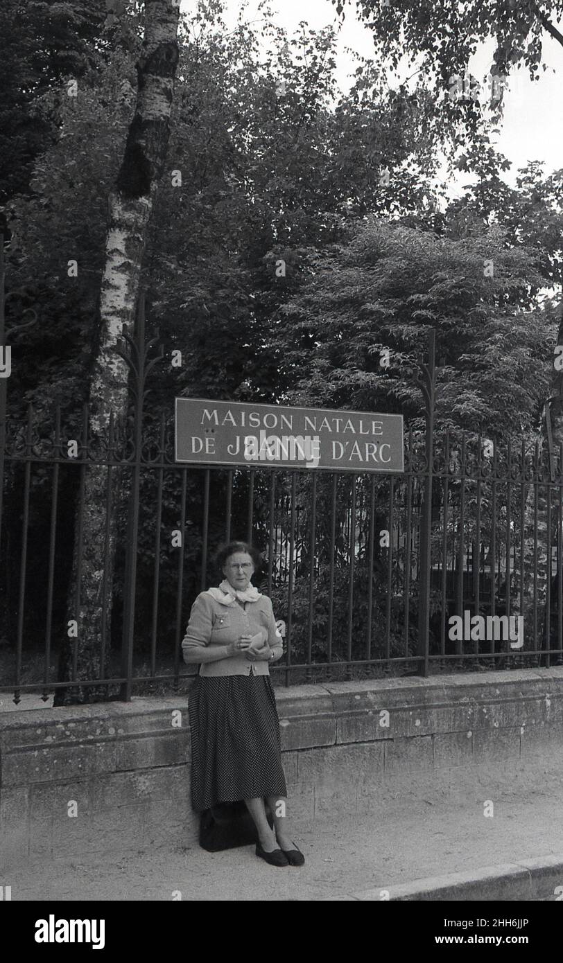1950s, historisch, eine Dame, die an einem Geländer unter einem Schild für das Maison Natale De Jeanne d'Arc in Domremy-la-Pucelle, Frankreich, steht, wo die französische Heldin Jeanne d'Arc zu Beginn des 15th. Jahrhunderts geboren wurde. Stockfoto