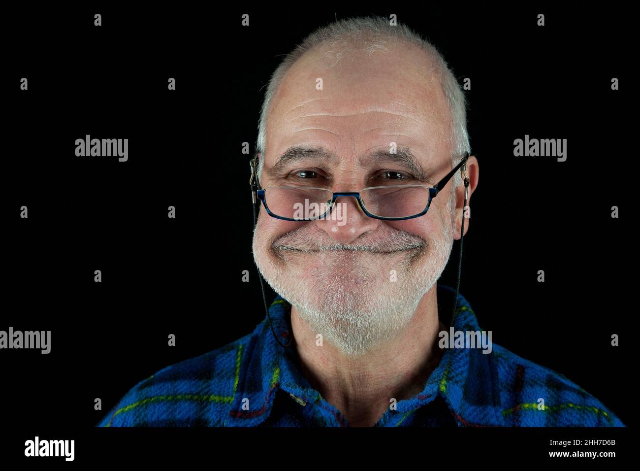 Der alte Mann mit Brille grinst vor schwarzem Hintergrund schelmisch an der Kamera. Stockfoto