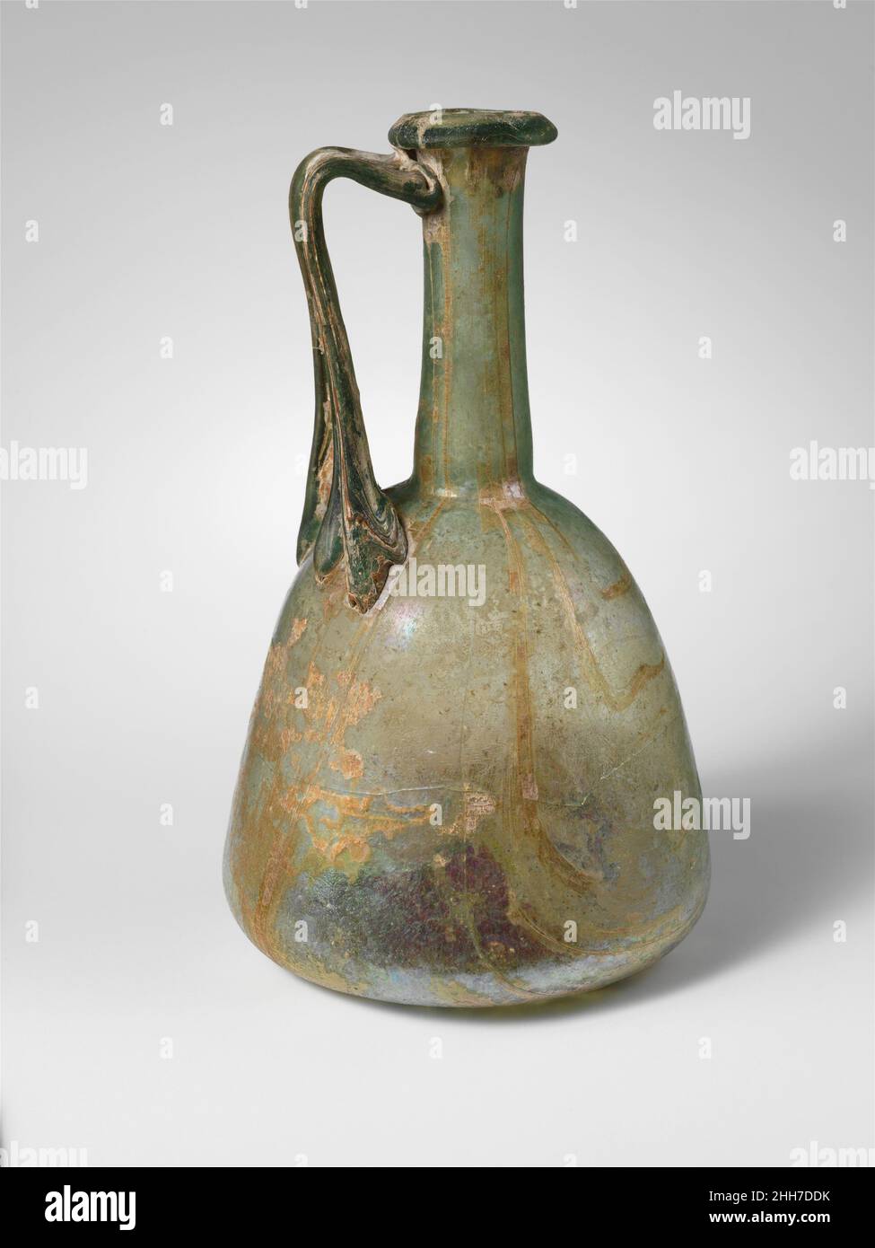 Glaskanne 1st–2nd century A.D. römisch Durchscheinend blaugrün; Griff in der gleichen Farbe.Rand ausgeklappt, nach unten, rund und innen, mit abgeschrägter Oberkante; hoher, schlanker zylindrischer Hals, leicht nach unten ausdehnend, mit Werkzeugeinrückung um den Boden; konischer Körper mit geschwungenen Seiten; fast flacher Boden; Dreirippiger Griff mit drei nach unten streckenden Krallen, der auf die Oberseite des Körpers aufgetragen wurde, nach oben gezogen und leicht nach außen gerichtet, horizontal gedreht und auf die Oberseite des Halses und der Unterseite von rim.Complete gezogen, jedoch mit einem großen Riss um den Körper und einem anderen quer über den Griff; einige Blasen und Blasstreifen; dul Stockfoto