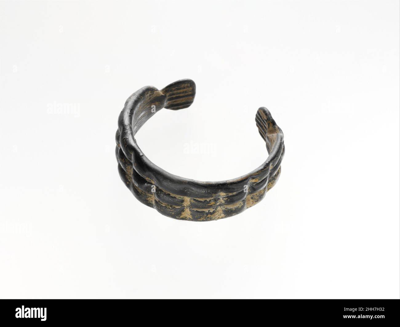 Glasarmband ca. 4th–5th. Jahrhundert n. Chr. römisch unsichere Farbe, undurchsichtiges Schwarz.dickes, offenes Band mit abgerundeten Kanten und sich nach den Enden verjüngenden Kanten.Außenfläche mit zwei tiefen parallelen Rillen, die horizontal entlang der Länge des Bandes verlaufen, die dann durch zehn vertikale Einbuchtung in Segmente unterteilt wird; Die Enden sind eingeklemmt und flach gepresst, mit regelmäßigen parallelen Linien im Relief auf beiden Oberflächen und erscheinen wie die Flossen oder der Schwanz eines Fisches.intakt; taumeln und viele Flecken bräunlicher Emaille-ähnlicher Verwitterung.Schwarzes Armband mit Kreuz und quer geformten Linien.. Armband aus Glas 239933 Stockfoto