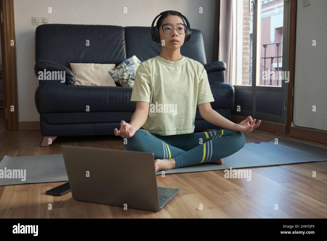 Junge asiatische Frau hört entspannende Musik und meditiert dabei die einfache Pose. Stockfoto